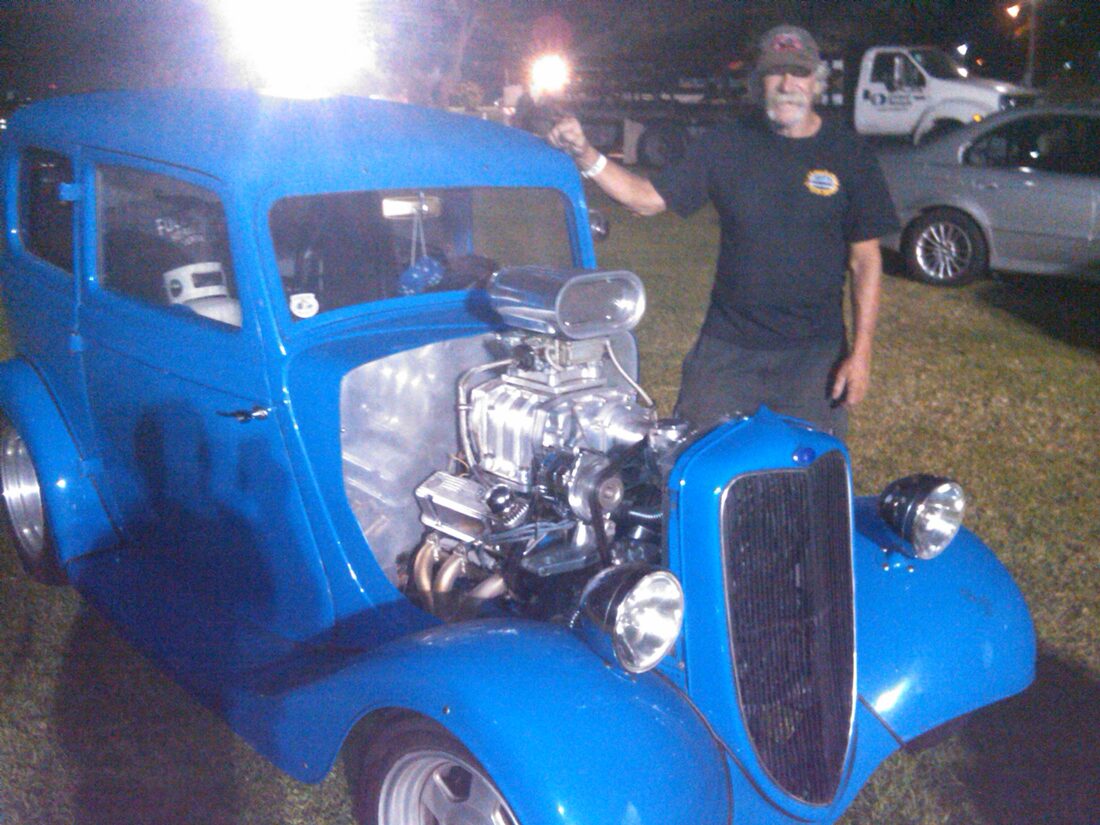 A performer beside a classic blue hot rod at the festival